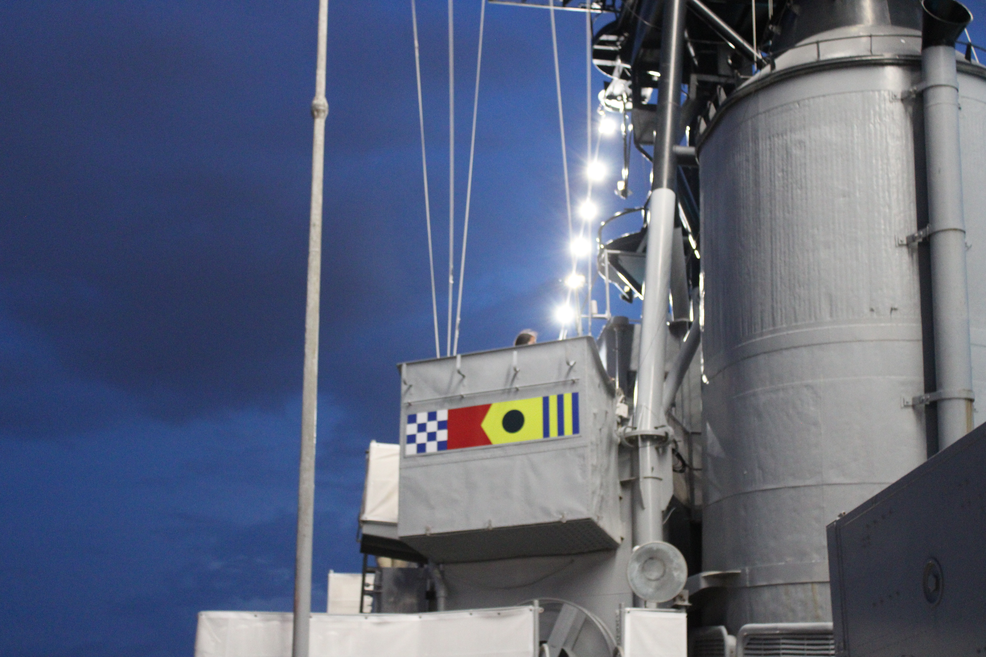 Signal flags illuminated on the USS Orleck superstructure against the evening sky