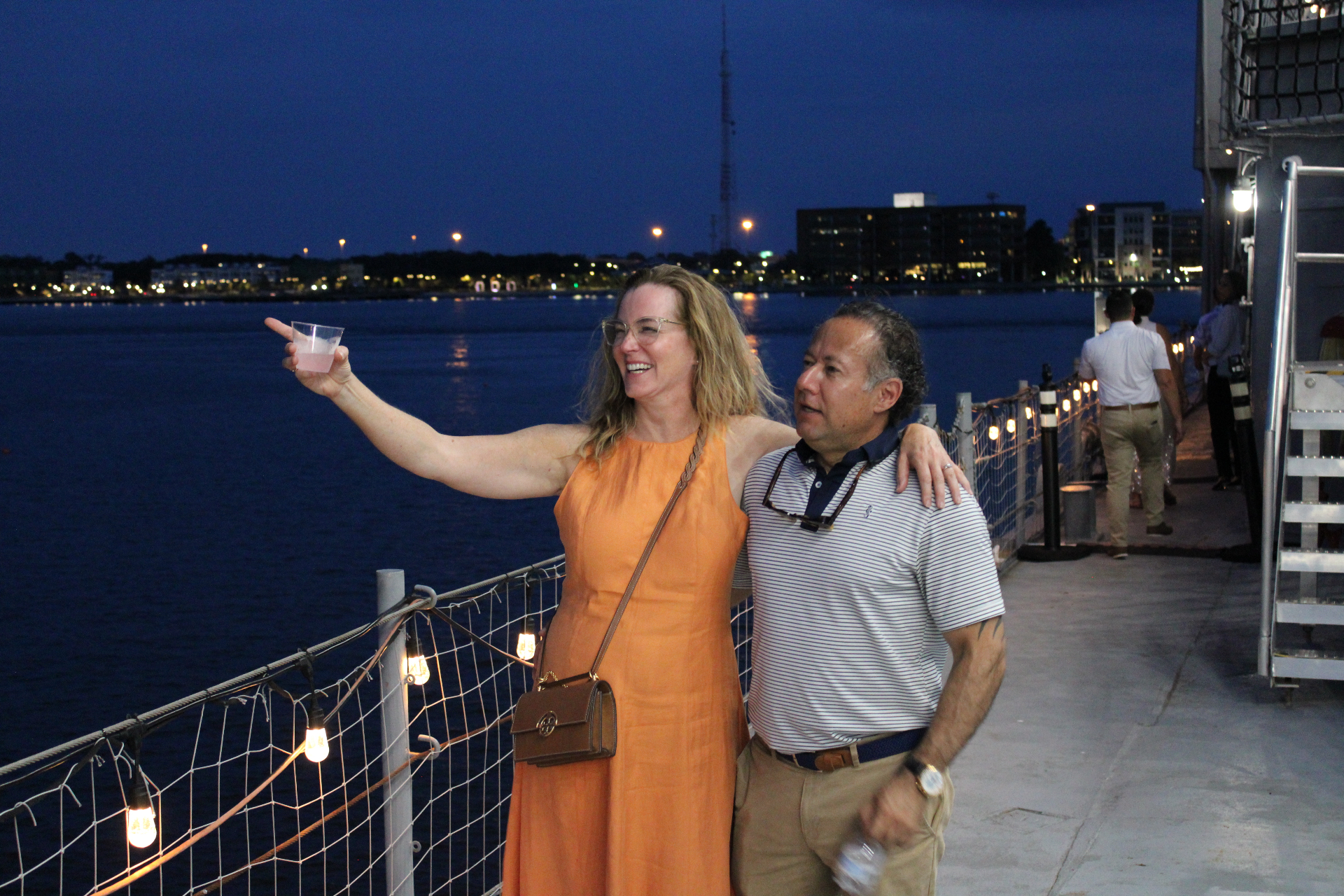 Couple toasting on the pier beside the USS Orleck at dusk with the Jacksonville riverfront lights across the St. Johns River
