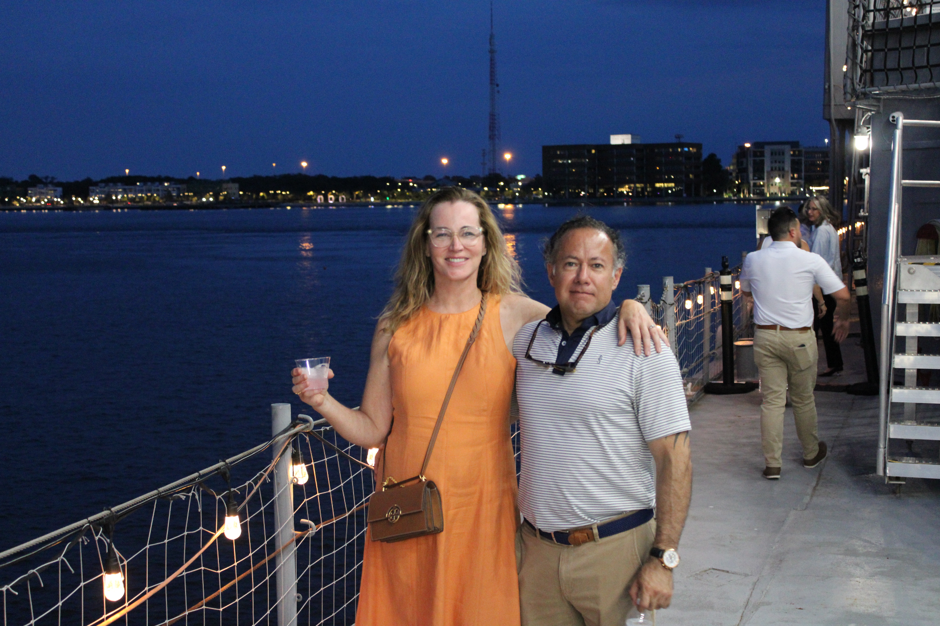 Couple posing on the USS Orleck deck at night with the Jacksonville riverfront lights behind them
