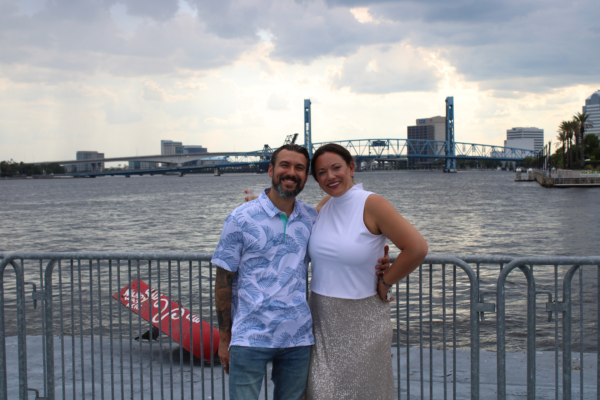 Couple smiling on the riverfront with the Main Street Bridge and downtown Jacksonville in the background