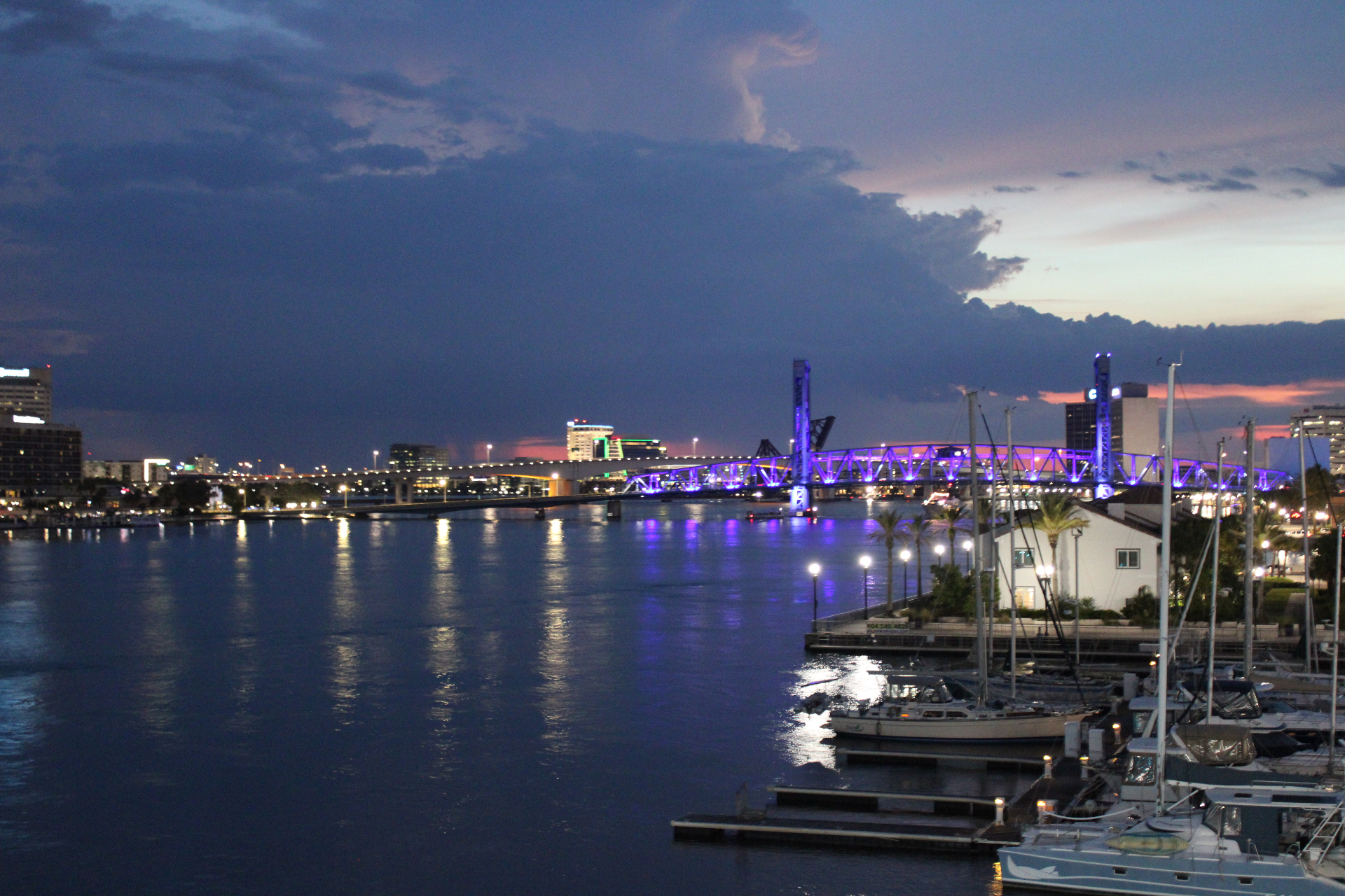 Downtown Jacksonville riverfront at dusk with the Main Street Bridge glowing purple and marina boats in the foreground