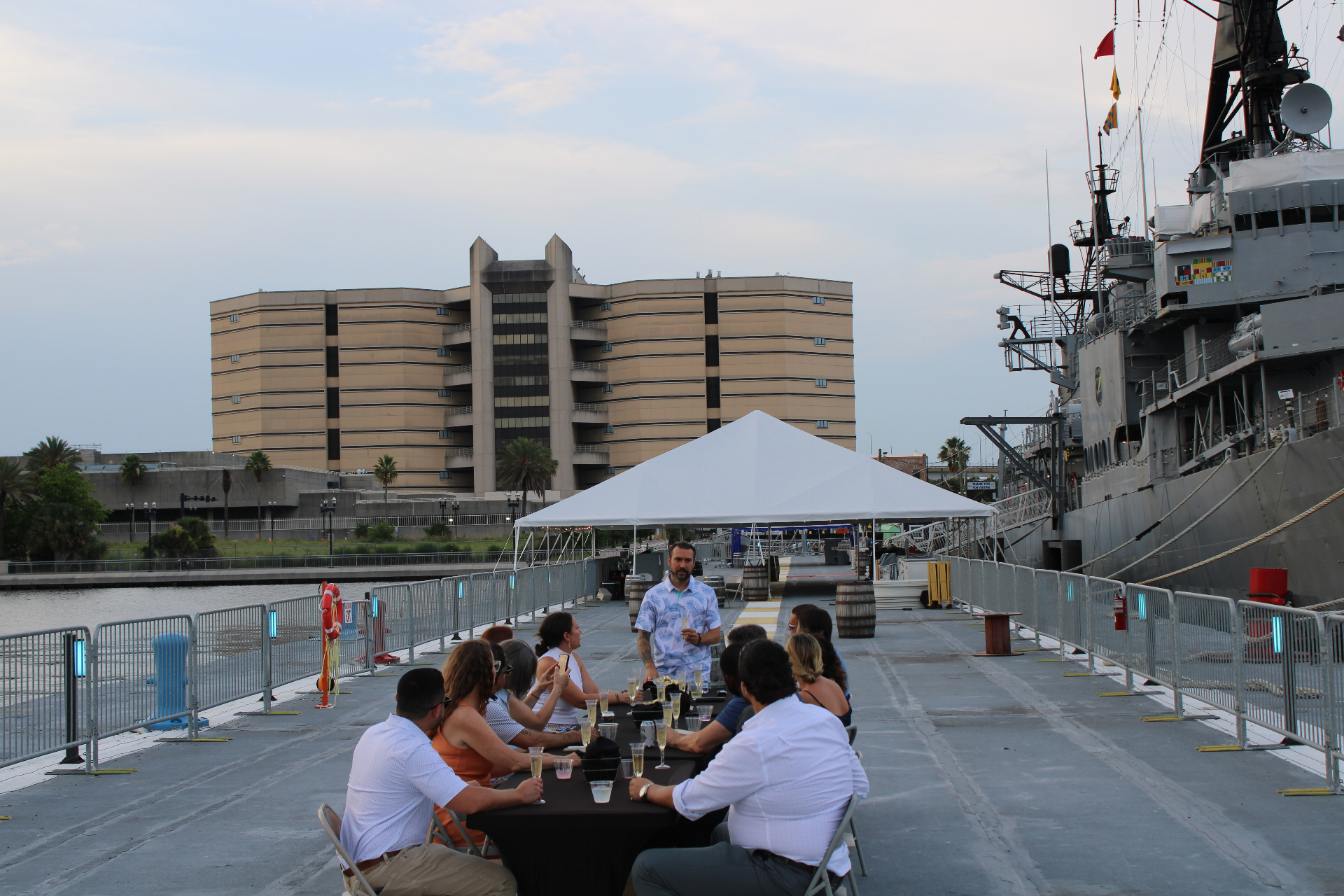 Guests gathered at a long dinner table on the pier beside the USS Orleck at sunset